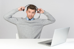 Call-center-agent zieht sein headset ab, während er am computer arbeitet
