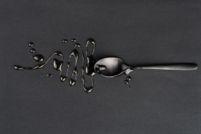 Metal tea spoon with liquid on the black