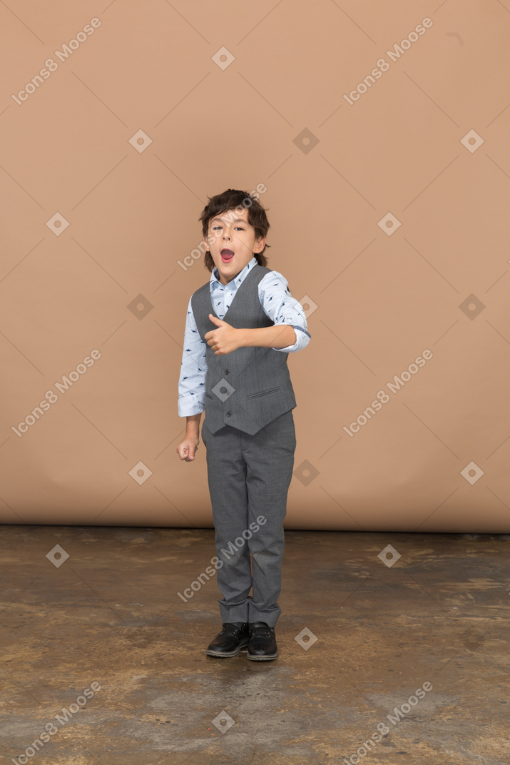 Front view of a cute boy in grey suit showing thumb up
