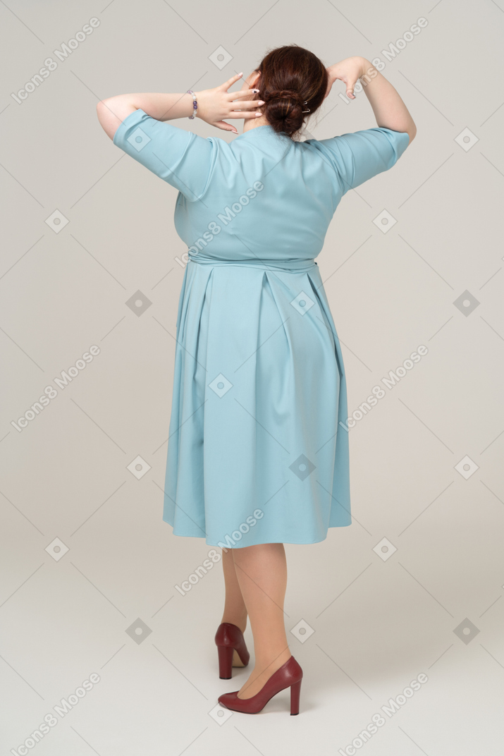 頭に手を置いて立っている青いドレスを着た女性の背面図