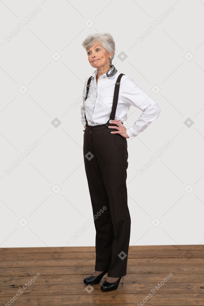 Vista de tres cuartos de una anciana en ropa de oficina poniendo las manos en las caderas