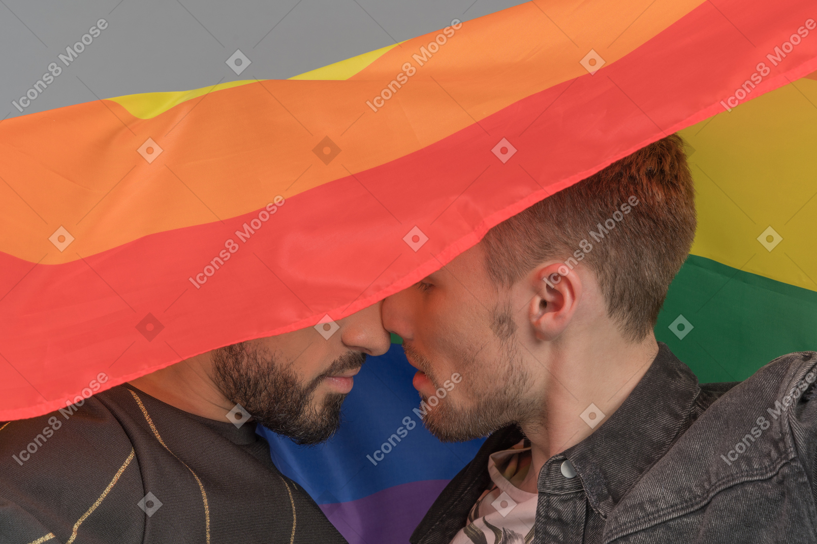 Primo piano di due giovani uomini che si toccano intimamente il naso sotto la bandiera lgbt