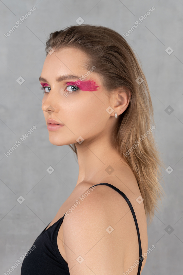 Young woman with bright pink eye make-up looking over shoulder