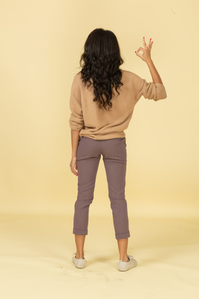 Vista de trás de uma jovem mulher de pele escura mostrando um gesto de ok