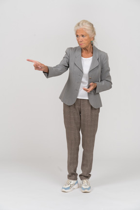 Вид спереди старушки в костюме, указывающей рукой