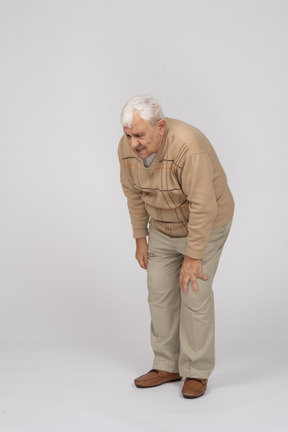 Vorderansicht eines alten mannes in freizeitkleidung, der sich nach unten beugt und sein schmerzendes knie berührt