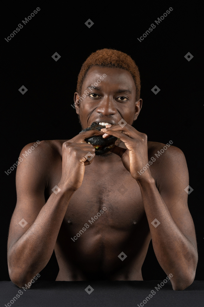 Vista frontal de un joven afro mordiendo una hamburguesa