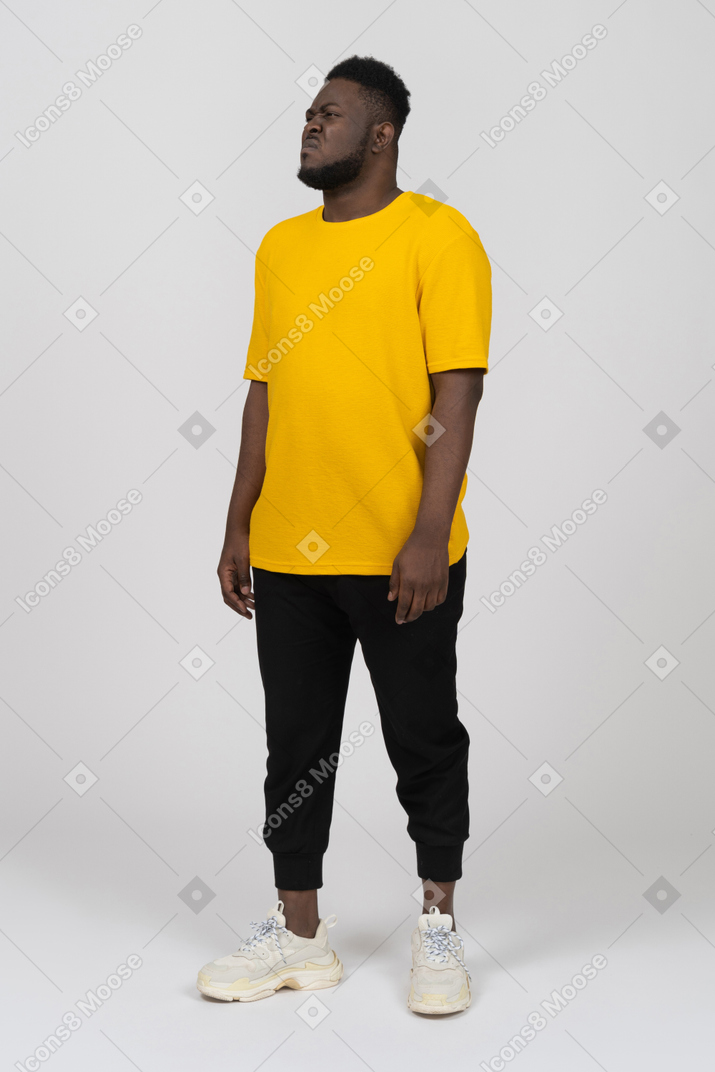 Vista de tres cuartos de un joven de piel oscura disgustado haciendo muecas en camiseta amarilla