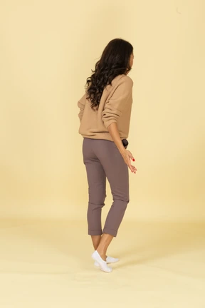 Three-quarter back view of a questioning dark-skinned young female leaning forward