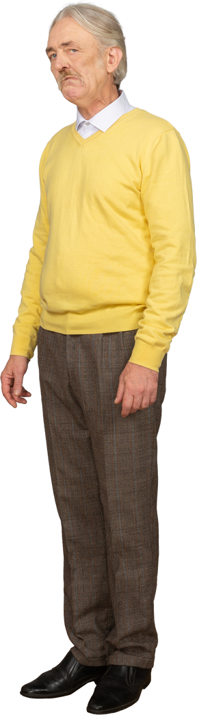 Vue de trois quarts d'un vieil homme triste dans un pull jaune regardant la caméra