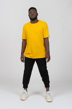 노란색 티셔츠를 입은 어두운 피부의 젊은 남자가 서 있는 모습