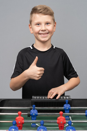 Front view of a boy playing foosball and showing thumb up