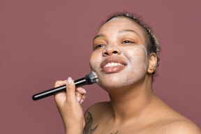 Улыбается афро-американских женщина, применяя крем для лица