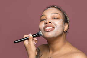 Sonriente mujer afroamericana aplicando una crema para la cara