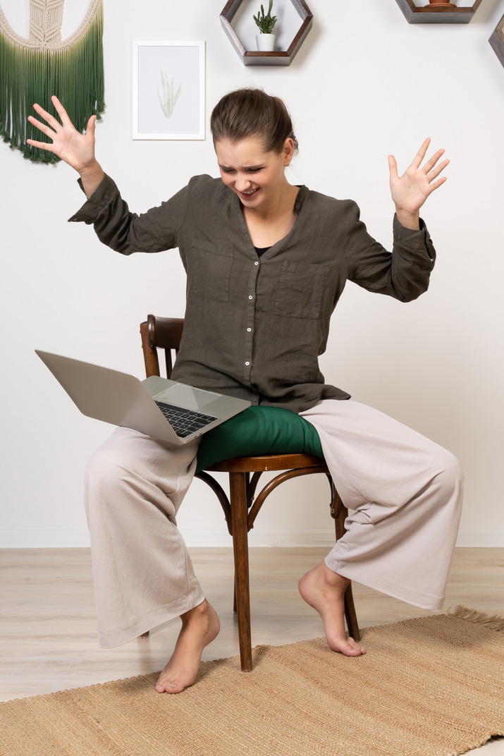 Front view of an irritated young woman with a headache sitting on a chair with a laptop