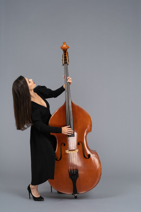 In voller länge einer jungen frau im schwarzen kleid, die kontrabass spielt, während sie sich zurücklehnt