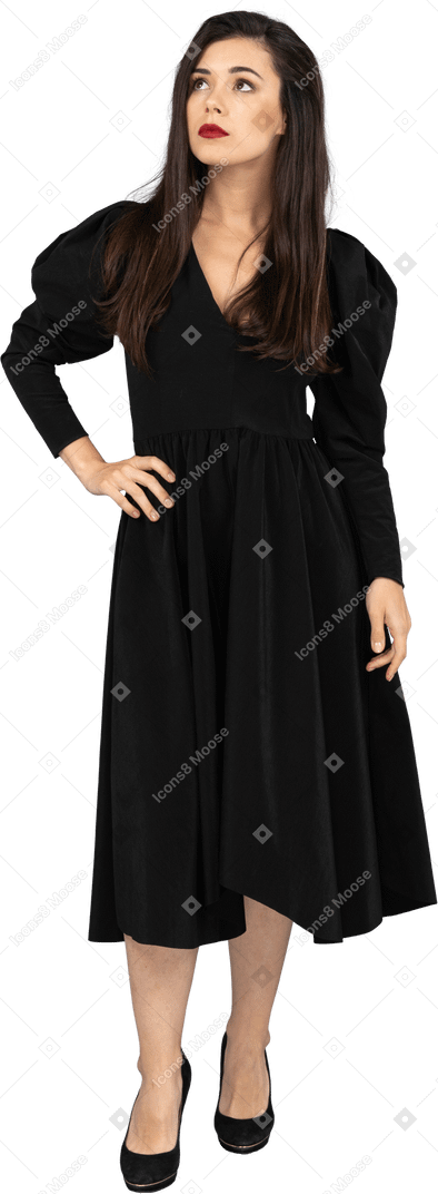 Vista frontal de uma jovem em um vestido preto colocando a mão no quadril