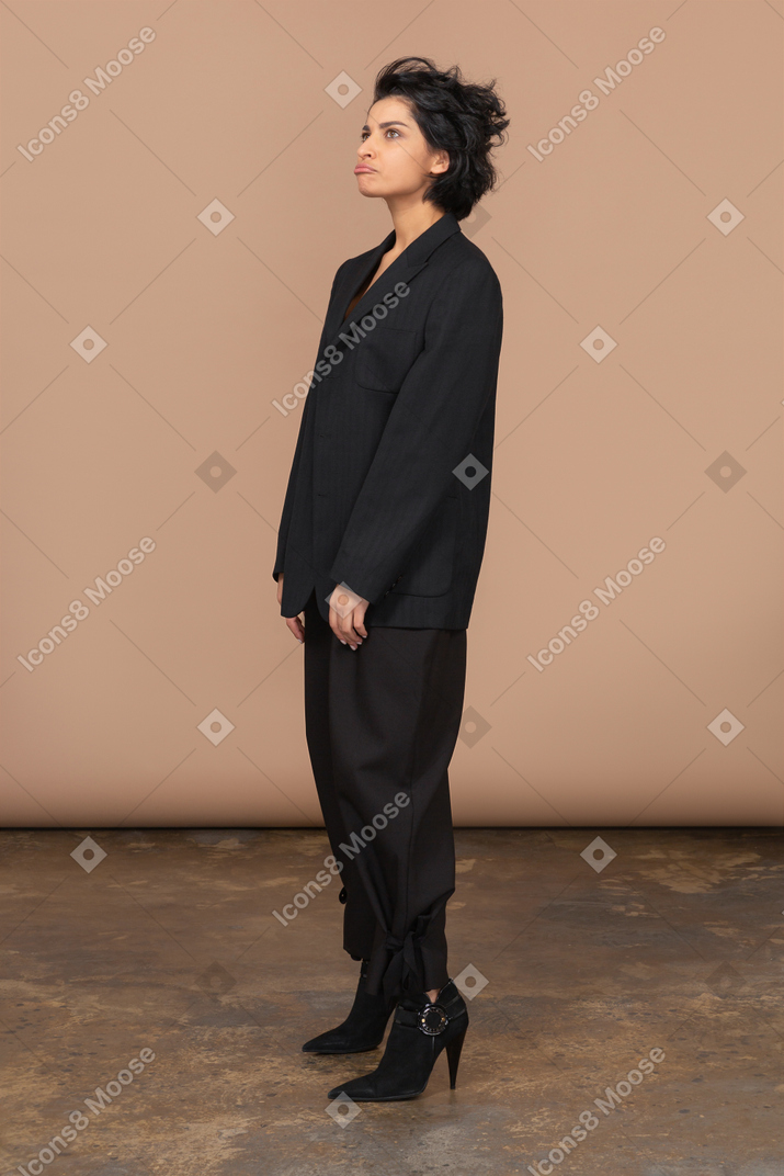 Vista de tres cuartos de una empresaria haciendo pucheros en un traje negro mirando hacia arriba con tristeza