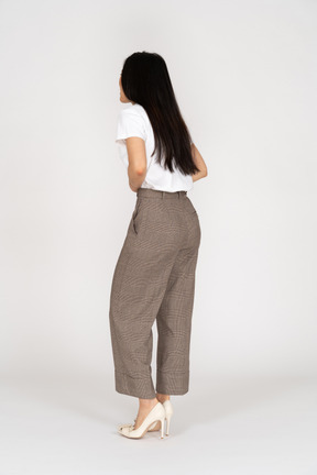 Vista posteriore di tre quarti di una giovane donna in calzoni e maglietta che si toccano lo stomaco