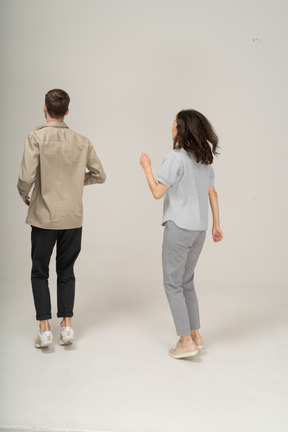 Three quarter back view of young man and woman jumping with raised hand