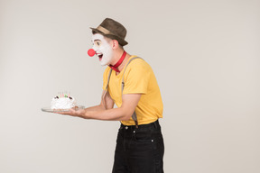 Male clown standing half sideways and holding a cake
