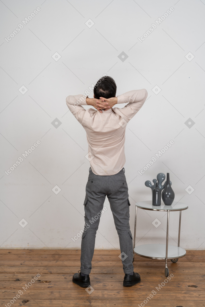 Вид сзади человека в повседневной одежде, стоящего с руками за головой