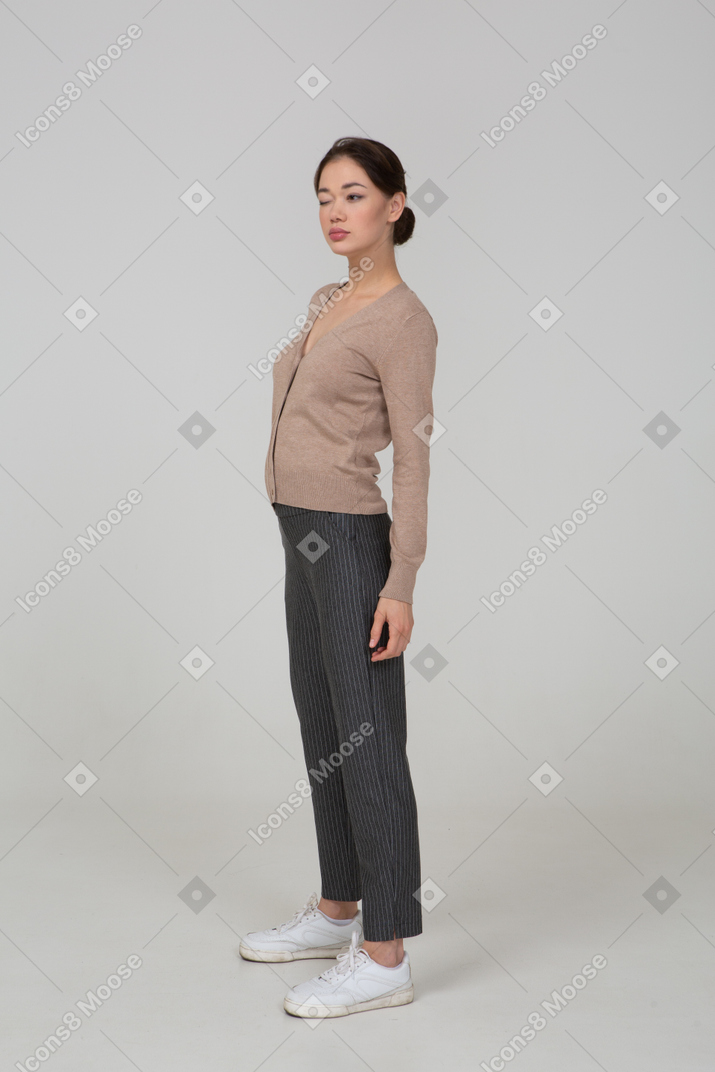 Three-quarter view of a winking young lady in pullover and pants putting hand on hip