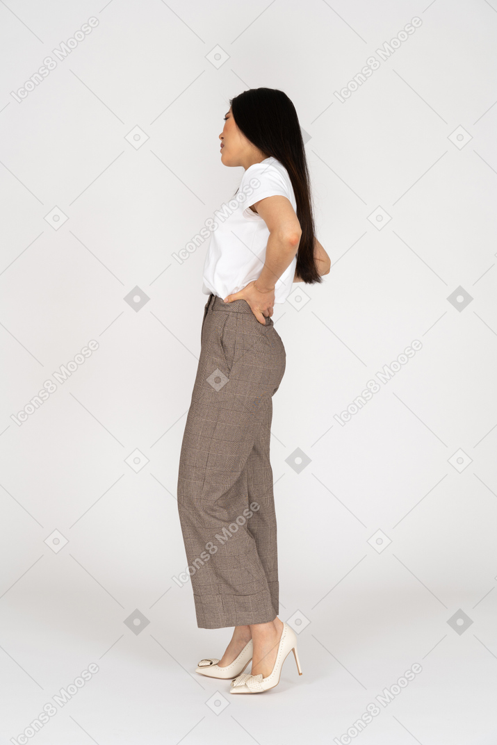 Vista lateral de uma jovem de calça e camiseta tocando suas costas
