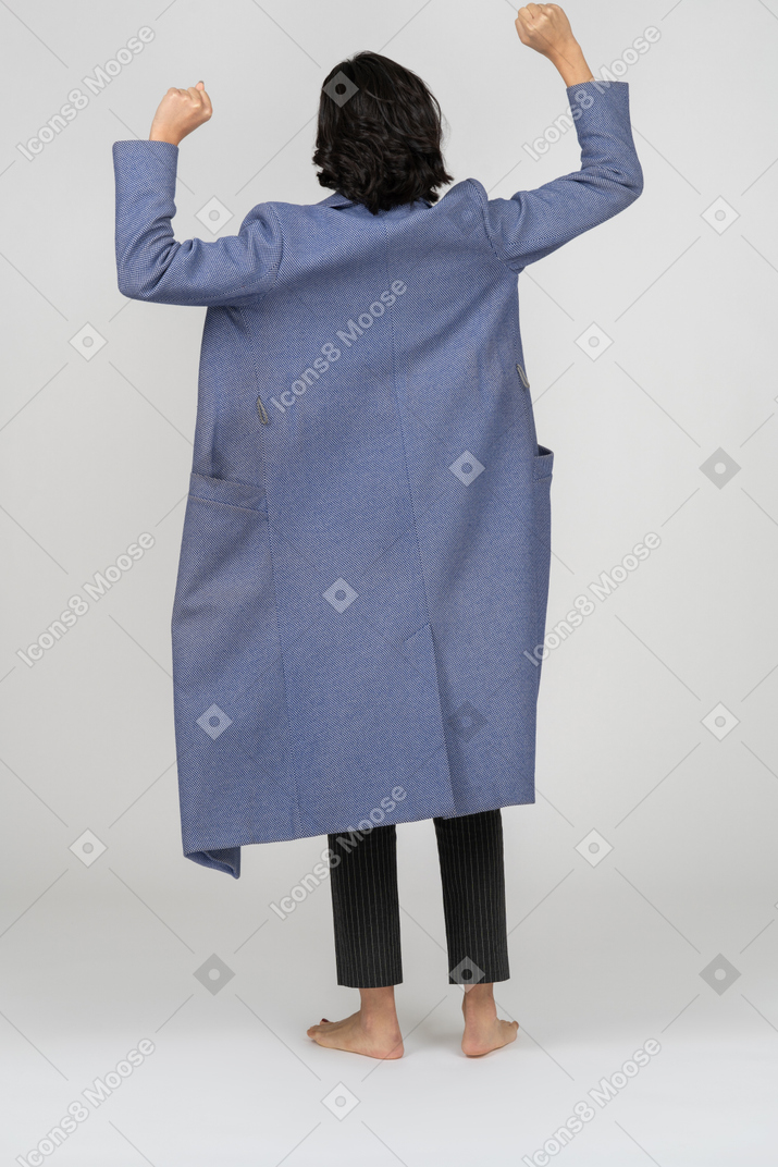Punto di vista posteriore di una donna in cappotto che esulta con le mani in alto