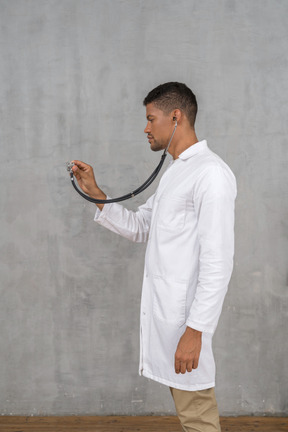 Vista lateral de un médico varón usando un estetoscopio