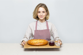 Menina segurando uma placa de corte com torta e geléia sobre ele