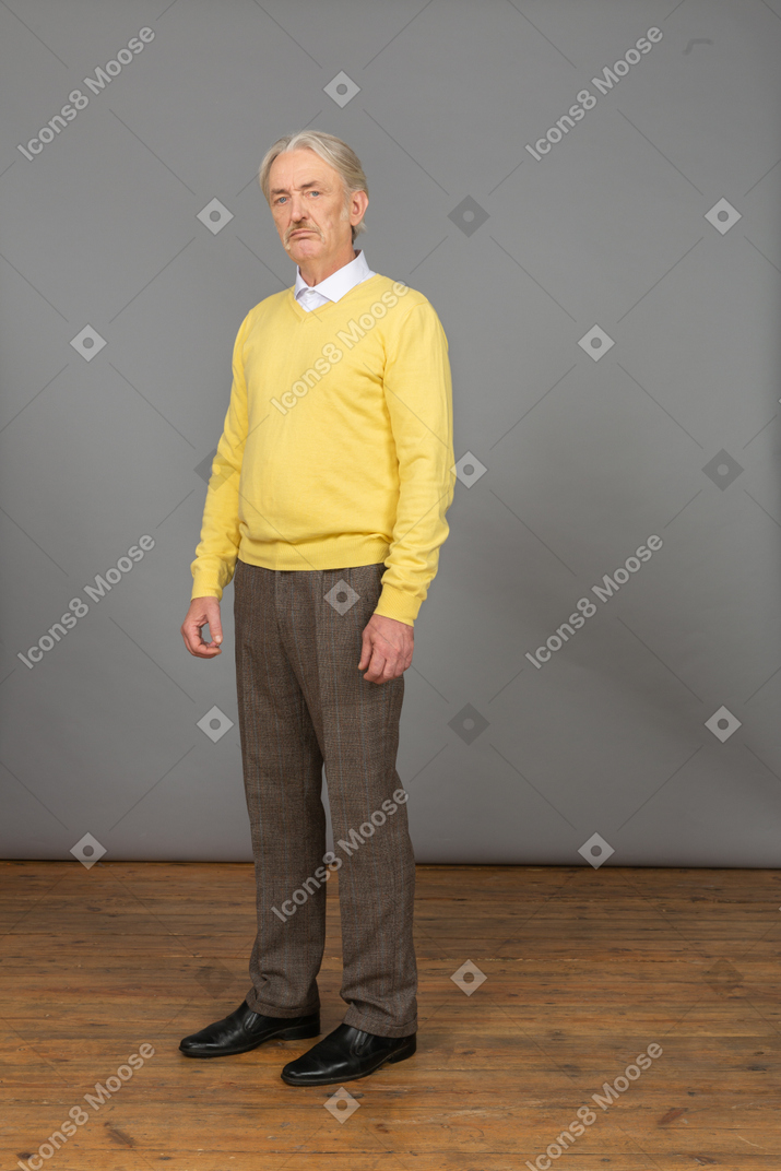 一个不高兴的老人，穿着黄色套头衫，看着相机的四分之三的视图