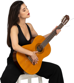 Vista di tre quarti di una giovane donna seduta in abito nero che tiene la chitarra con gli occhi chiusi