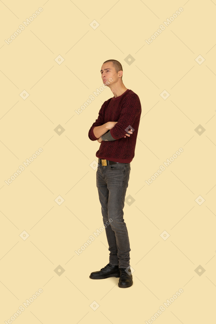 Three-quarter view of an offended young man dressed in casual clothes crossing his hands