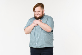 Um homem gordo sorrindo timidamente com as mãos no peito