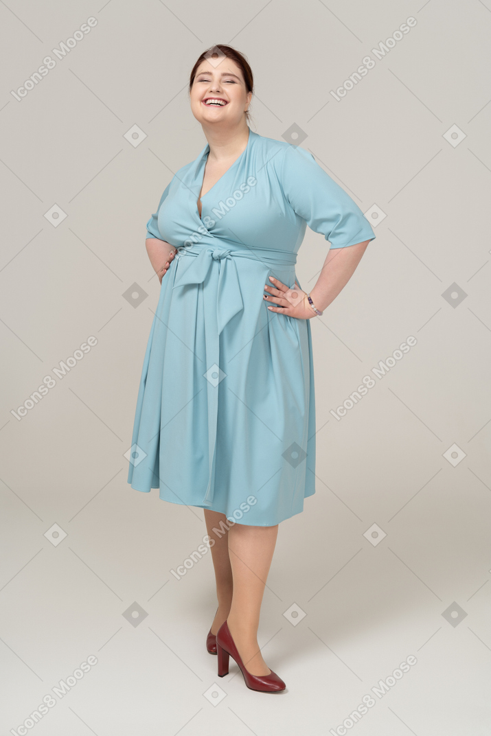 Vista frontale di una donna felice in abito blu in piedi con le mani sui fianchi