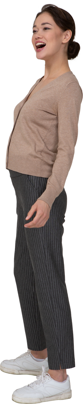 Vista di tre quarti di una donna che ride in pullover e pantaloni mettendo la mano sul fianco