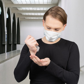 Un giovane in una maschera con un disinfettante per le mani