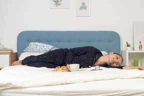 Vista frontal de uma jovem deitada na cama tomando café da manhã