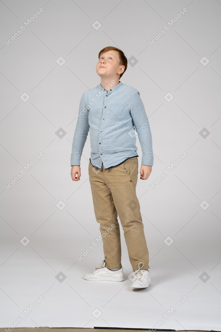 Menino de camisa azul em pé e olhando para cima