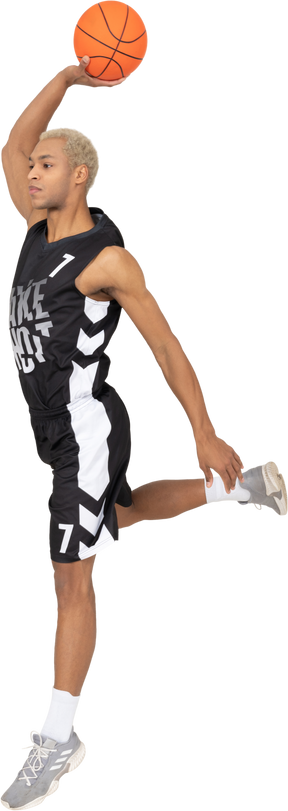 Vista laterale di un giovane giocatore di basket maschile che segna un punto