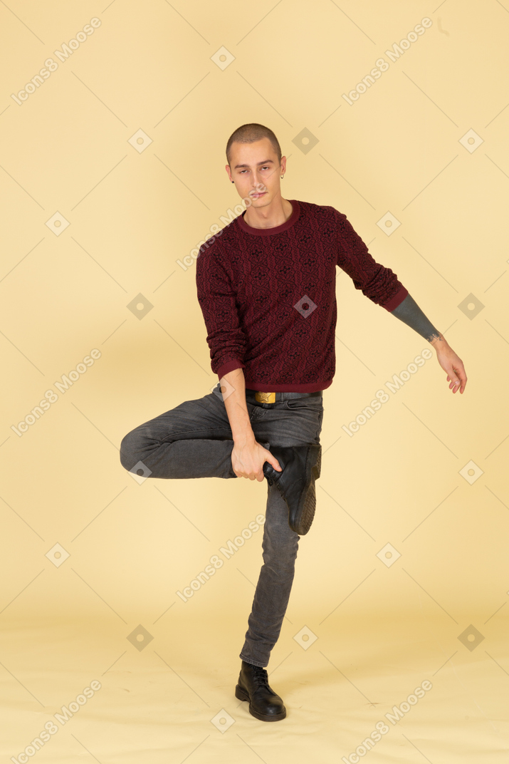 Vista frontal de um jovem cansado de pulôver vermelho tocando seu tornozelo