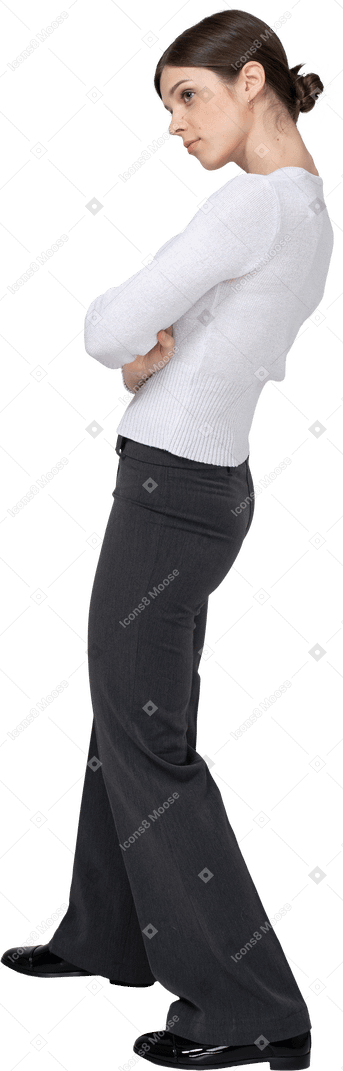 Vista posterior de tres cuartos de una mujer joven en ropa de oficina cruzando los brazos