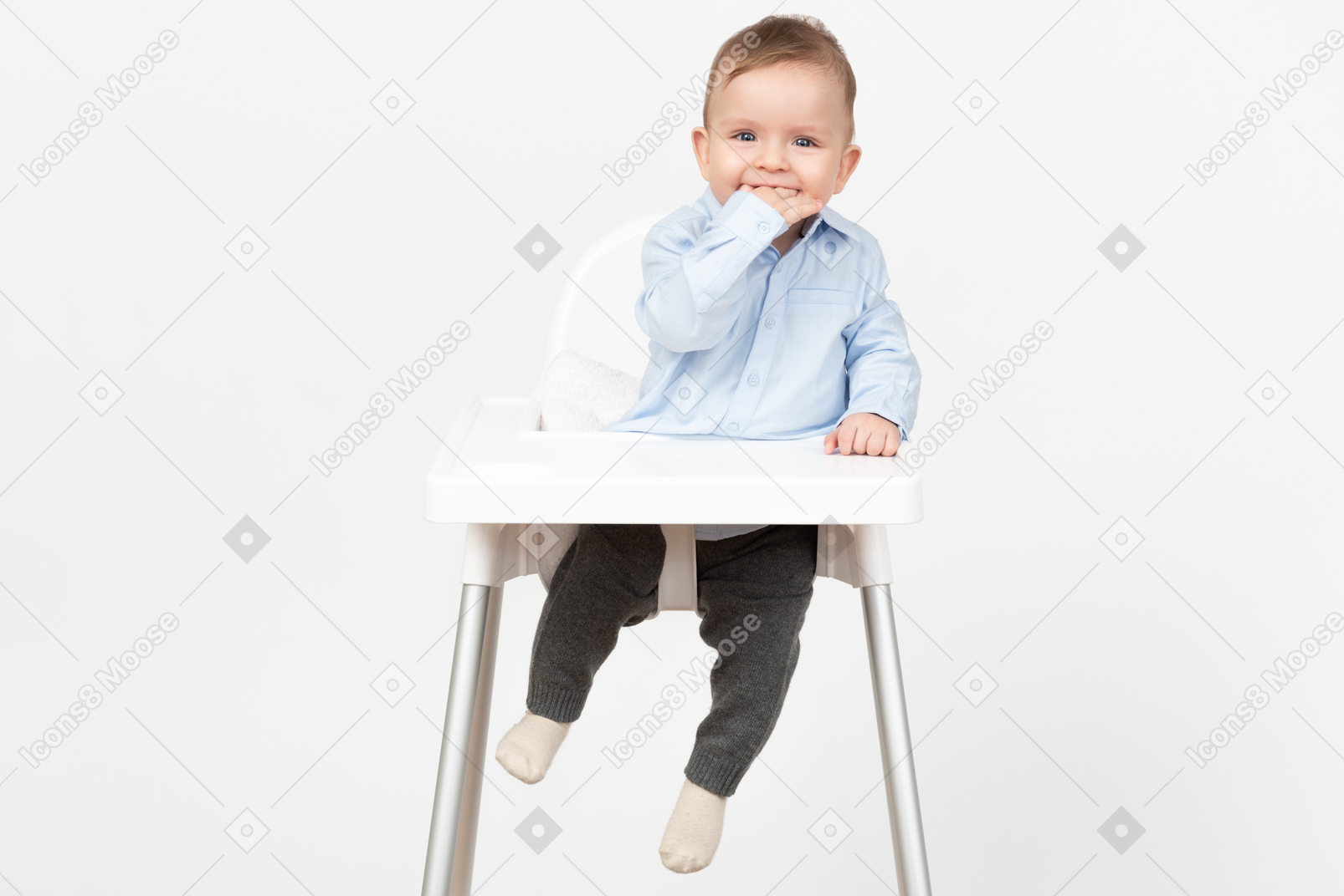 Adorable baby boy sitting in highchair and holding hand in mouth