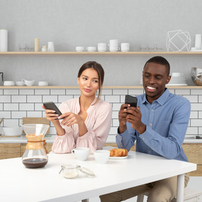 A man and a woman sitting at a table looking at their cell phones