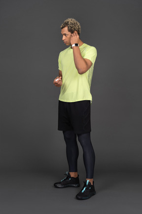 Three-quarter view of a dark-skinned young man putting on an earphone