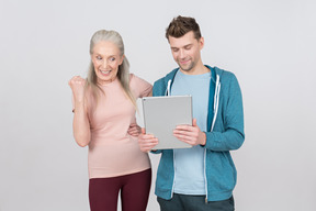 Excitada anciana y chico joven mirando los resultados deportivos en la tableta