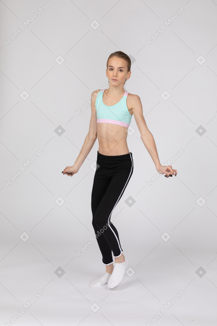 Vista de tres cuartos de una tímida jovencita en ropa deportiva extendiendo las manos y mirando a la cámara