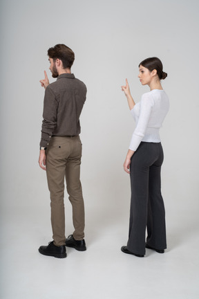 Vista traseira a três quartos de um jovem casal com roupas de escritório, levantando o dedo