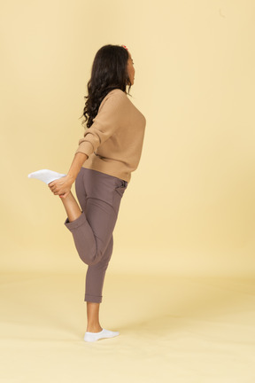 Vista lateral de una mujer joven de piel oscura tocando su pierna y tobillo